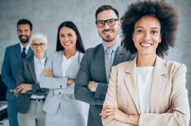 Portrait of beautiful smiling businesswoman with her colleagues. Multi-ethnic group of business persons standing in a row in modern office. Successful team leader and her team in background.